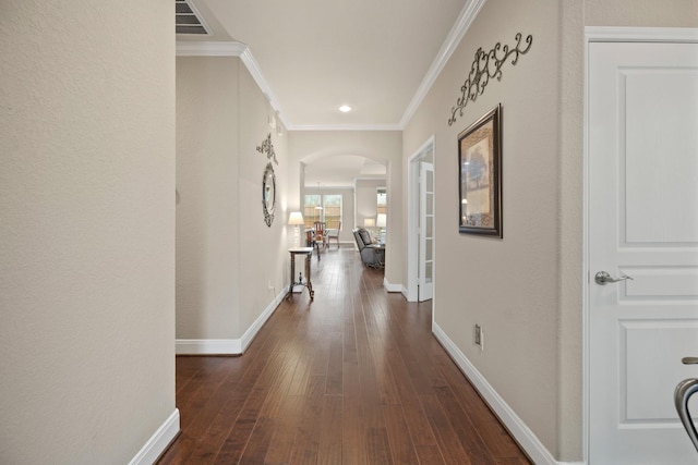 hallway featuring visible vents, arched walkways, baseboards, wood-type flooring, and ornamental molding