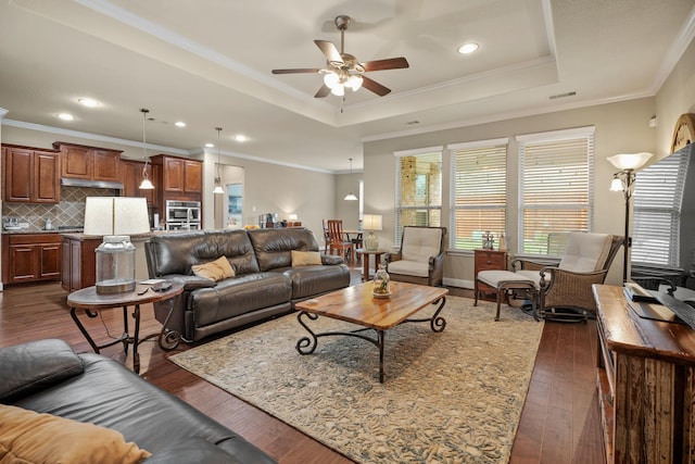 living area with dark wood-style flooring, a raised ceiling, visible vents, and crown molding