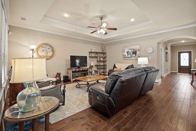 living room with dark wood-style floors, a tray ceiling, visible vents, and arched walkways