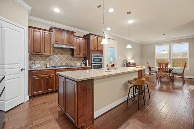 kitchen with under cabinet range hood, stainless steel appliances, dark wood-type flooring, a kitchen island, and visible vents