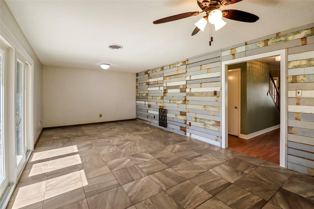 spare room featuring wood walls, visible vents, and baseboards