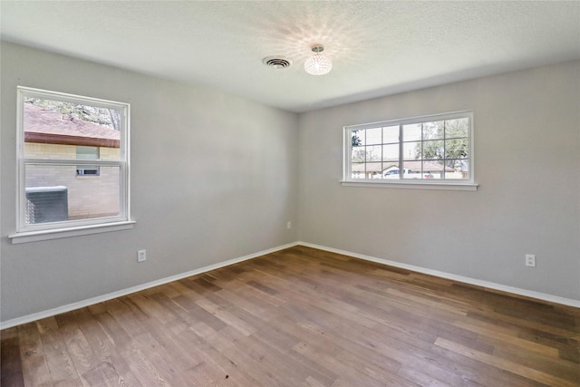 empty room featuring baseboards, wood finished floors, visible vents, and a healthy amount of sunlight