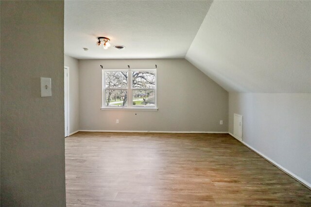 bonus room featuring a textured ceiling, vaulted ceiling, wood finished floors, and visible vents