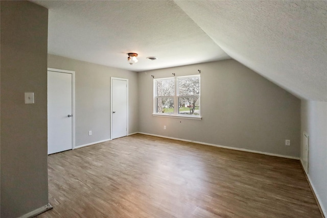 additional living space featuring a textured ceiling, vaulted ceiling, wood finished floors, and visible vents