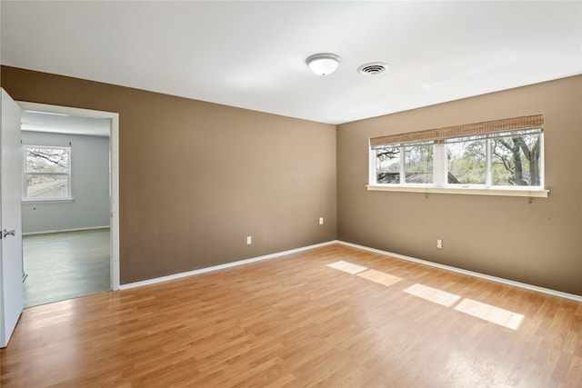 unfurnished room with light wood-style floors, visible vents, and baseboards