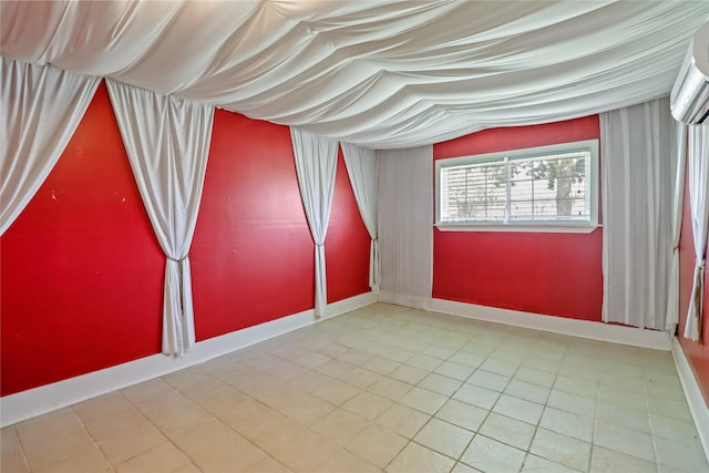 tiled spare room with a wall unit AC and baseboards