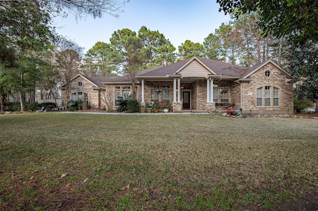 view of front of house with covered porch, a front lawn, roof with shingles, and brick siding