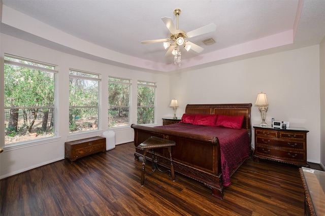 bedroom with wood finished floors, a raised ceiling, visible vents, and a ceiling fan