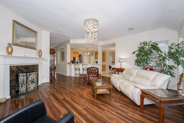 living room with dark wood-style flooring, a fireplace, a notable chandelier, visible vents, and vaulted ceiling