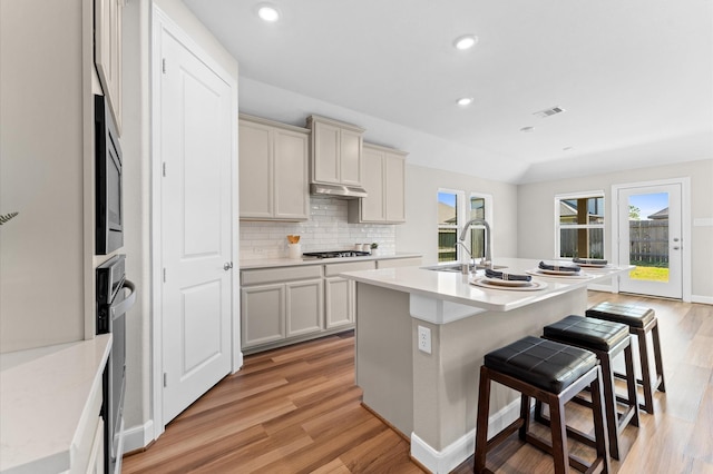 kitchen featuring light wood finished floors, visible vents, decorative backsplash, a breakfast bar, and a sink