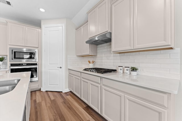 kitchen with under cabinet range hood, visible vents, appliances with stainless steel finishes, light wood-type flooring, and decorative backsplash