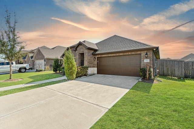 view of front of home with brick siding, a yard, fence, a garage, and driveway