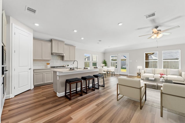 kitchen with a center island with sink, visible vents, open floor plan, and backsplash