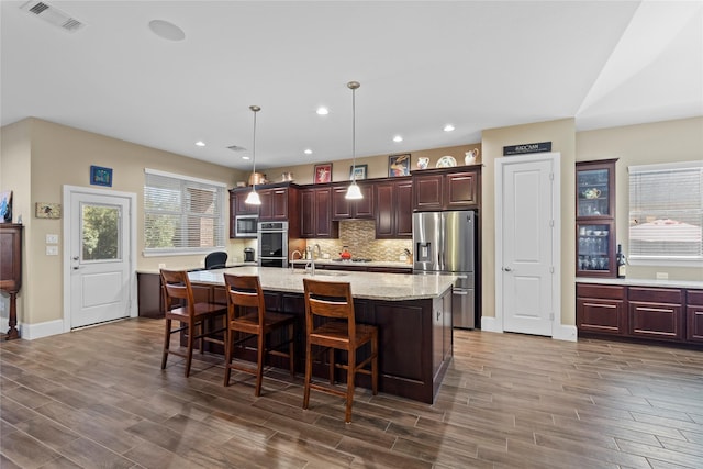 kitchen featuring a breakfast bar, wood finish floors, appliances with stainless steel finishes, tasteful backsplash, and an island with sink