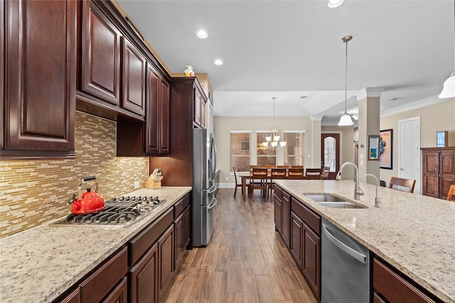 kitchen featuring stainless steel appliances, a sink, backsplash, light stone countertops, and decorative light fixtures