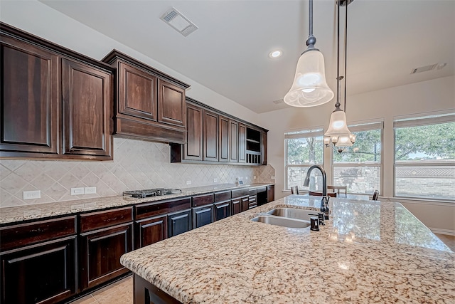 kitchen featuring light stone counters, backsplash, a sink, and visible vents