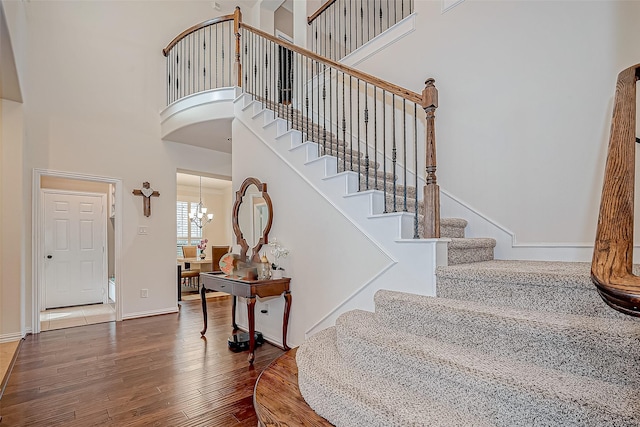 foyer featuring baseboards, a towering ceiling, wood finished floors, stairs, and a chandelier