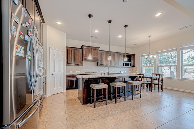 kitchen featuring decorative backsplash, a kitchen breakfast bar, freestanding refrigerator, dark brown cabinets, and pendant lighting