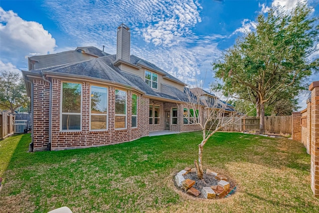 rear view of house with a chimney, brick siding, a yard, and a fenced backyard