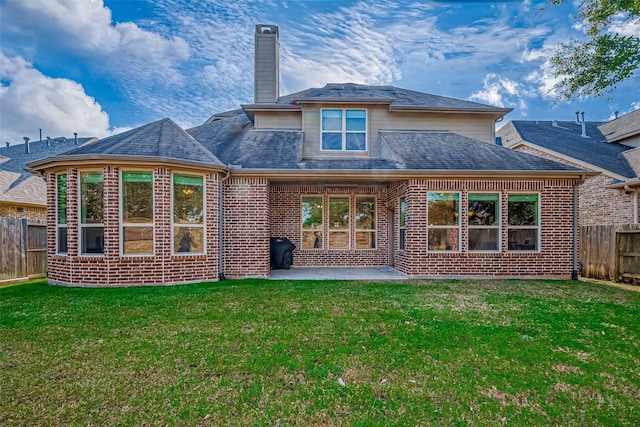 rear view of property with brick siding, fence, a lawn, a chimney, and a patio area