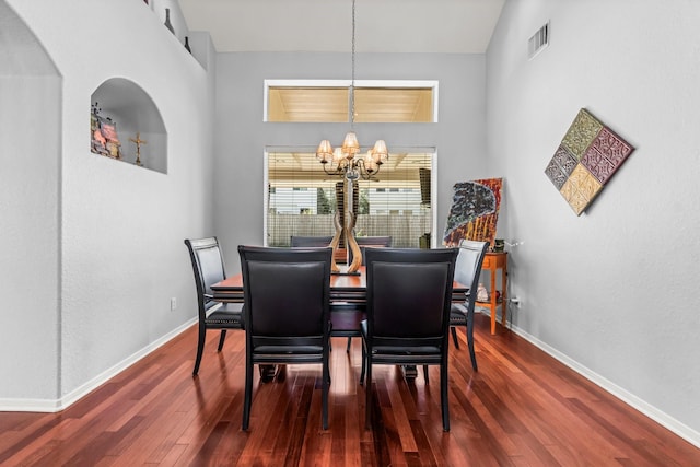 dining room with visible vents, a notable chandelier, hardwood / wood-style flooring, baseboards, and a towering ceiling