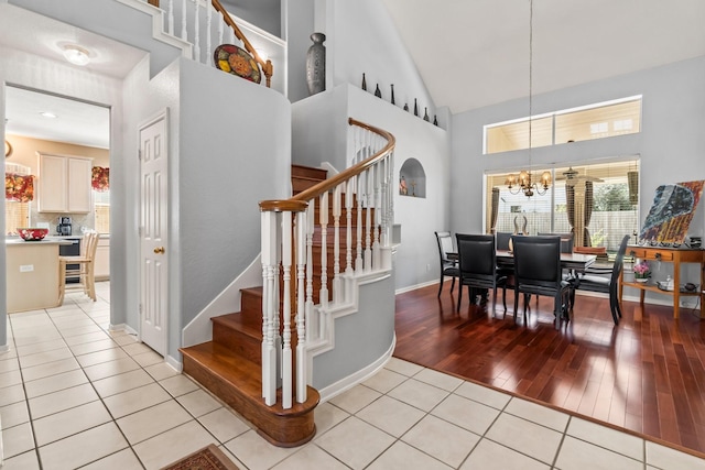 dining space featuring stairs, an inviting chandelier, light tile patterned flooring, and high vaulted ceiling