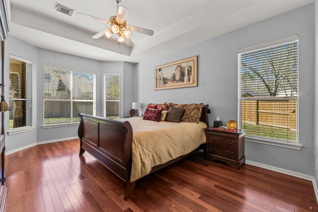 bedroom with visible vents, a tray ceiling, baseboards, and dark wood-style flooring