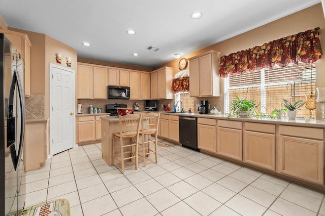 kitchen featuring tasteful backsplash, light brown cabinets, a center island, black appliances, and a sink