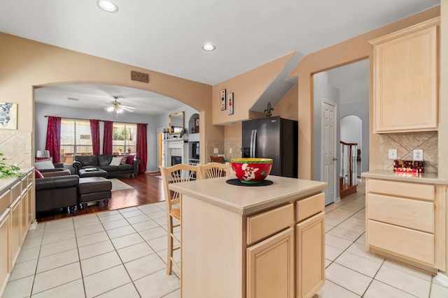 kitchen with a fireplace, light brown cabinets, stainless steel fridge, and arched walkways