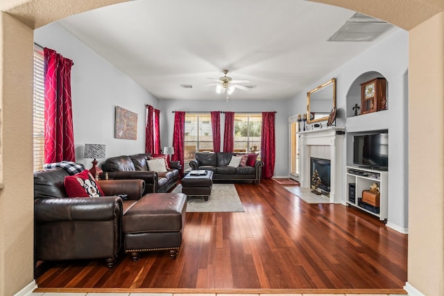 living area with visible vents, a ceiling fan, a tiled fireplace, hardwood / wood-style floors, and baseboards