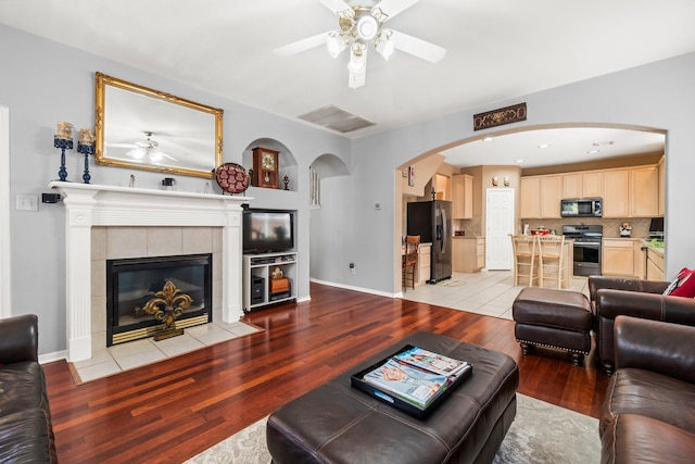 living room with visible vents, light wood-style flooring, a fireplace, baseboards, and ceiling fan