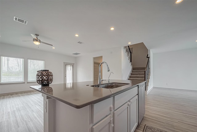 kitchen featuring light wood-style flooring, a sink, visible vents, dishwasher, and dark countertops