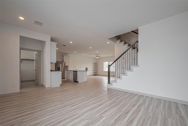 unfurnished living room with light wood finished floors, visible vents, stairway, and recessed lighting