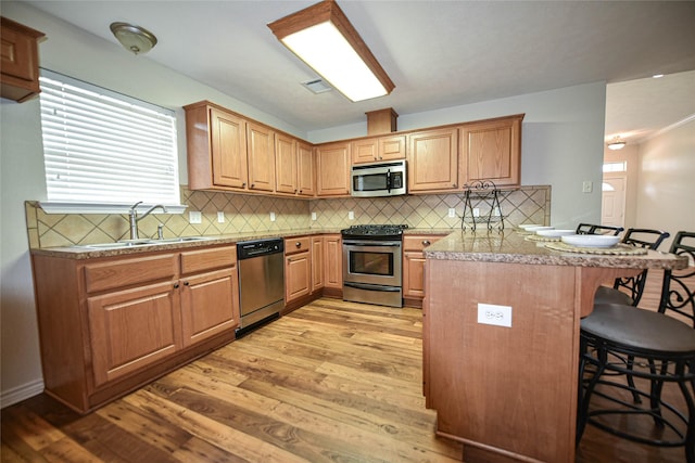 kitchen with light wood finished floors, appliances with stainless steel finishes, a peninsula, a kitchen bar, and a sink