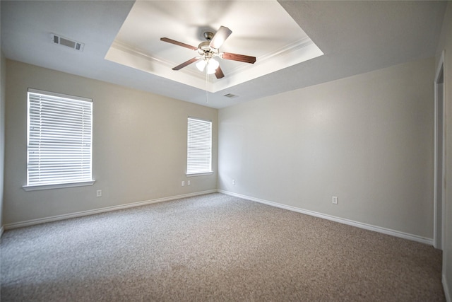 spare room featuring carpet floors, a raised ceiling, visible vents, ornamental molding, and baseboards