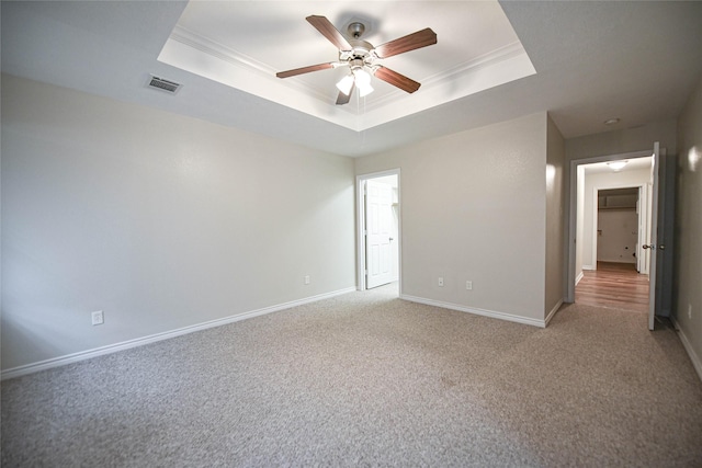 spare room featuring light colored carpet, visible vents, baseboards, ornamental molding, and a tray ceiling