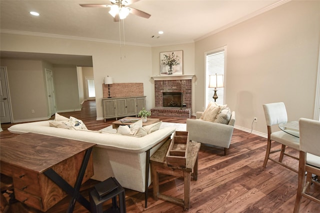 living area with a ceiling fan, baseboards, a brick fireplace, dark wood-style floors, and crown molding