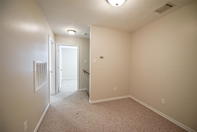 corridor with baseboards, visible vents, a textured ceiling, and light colored carpet