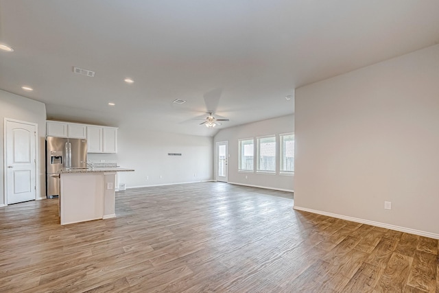 interior space with light wood-type flooring, ceiling fan, visible vents, and baseboards