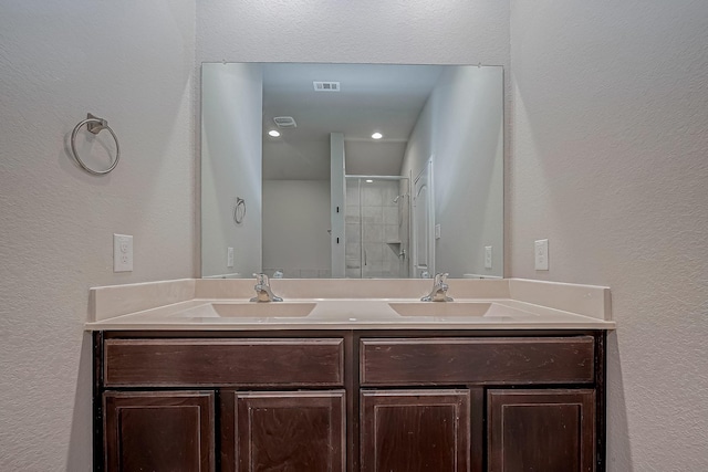 full bathroom with double vanity, a shower stall, visible vents, and a sink