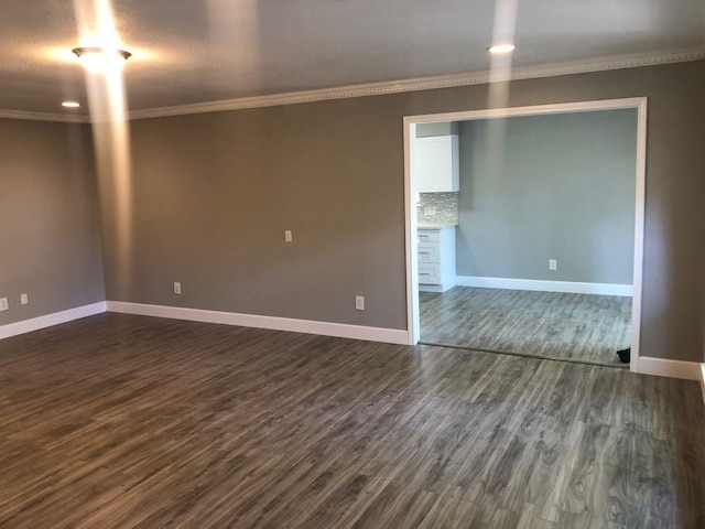 spare room featuring baseboards, dark wood finished floors, and crown molding