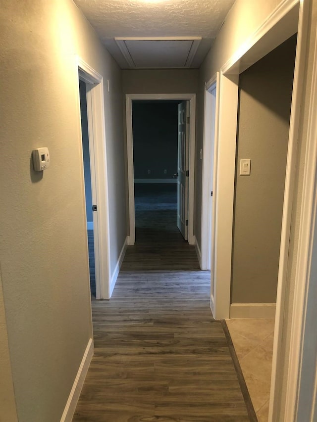 corridor with a textured ceiling, baseboards, and wood finished floors