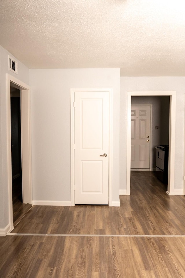 spare room featuring baseboards, wood finished floors, visible vents, and a textured ceiling