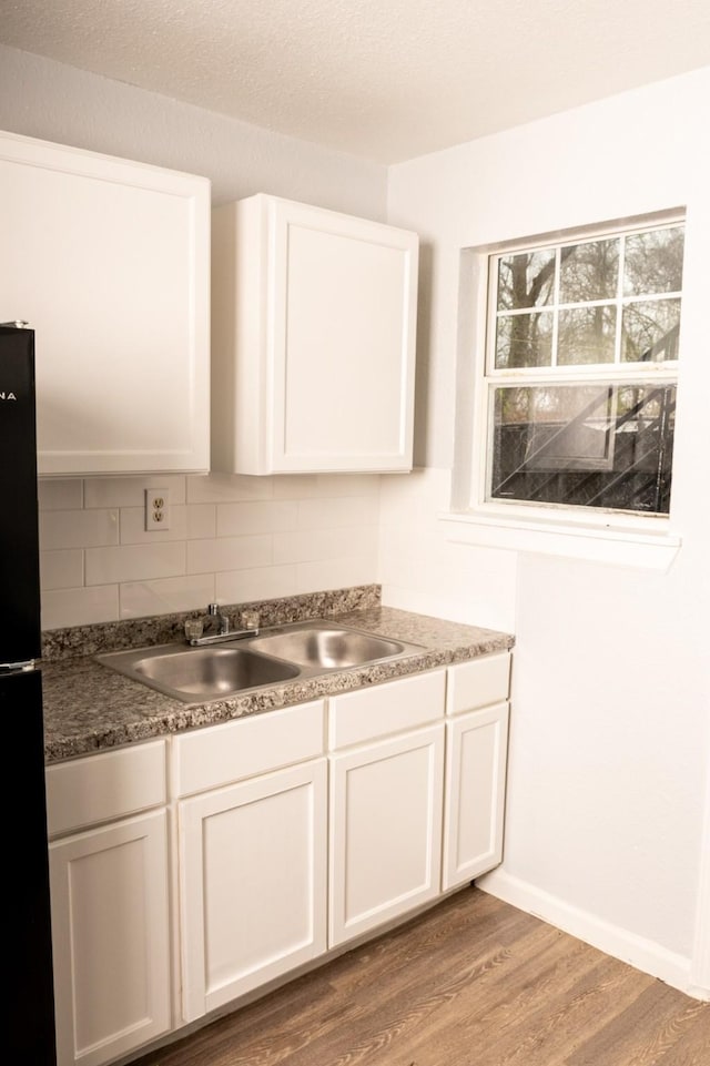 kitchen with light wood-style flooring, white cabinetry, freestanding refrigerator, and a sink