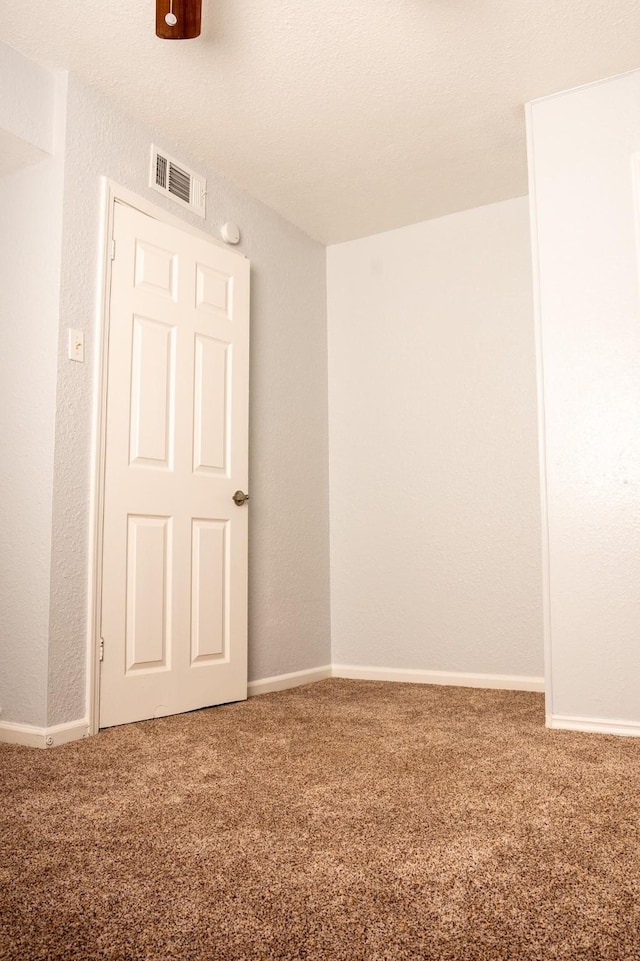 carpeted empty room with baseboards, visible vents, and a textured wall