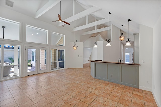 unfurnished living room featuring a ceiling fan, beam ceiling, plenty of natural light, and french doors