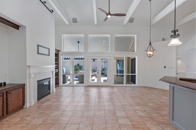 unfurnished living room with a ceiling fan, beam ceiling, light tile patterned flooring, a fireplace, and french doors