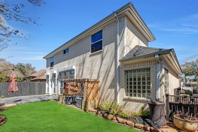 back of house featuring a patio, fence, a yard, roof with shingles, and brick siding