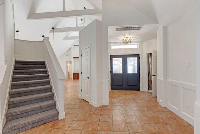 entrance foyer with a wainscoted wall, visible vents, arched walkways, stairs, and a decorative wall