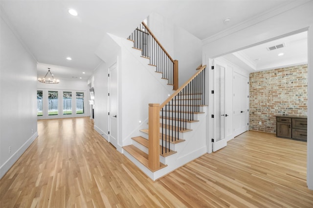 stairway with a notable chandelier, visible vents, crown molding, and wood finished floors